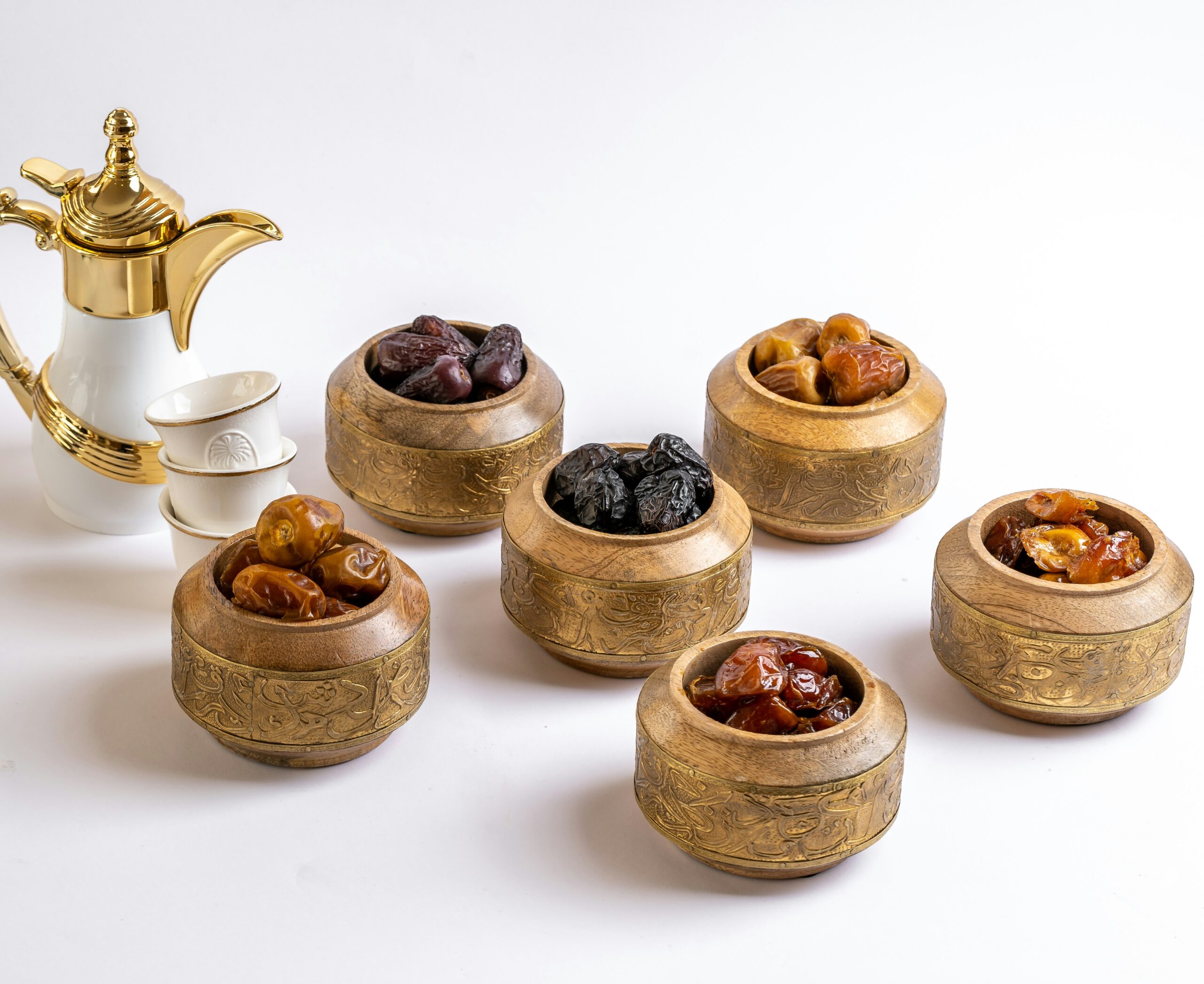 Assorted dates in wooden bowls beside Arabic coffee cups and a golden coffee pot
