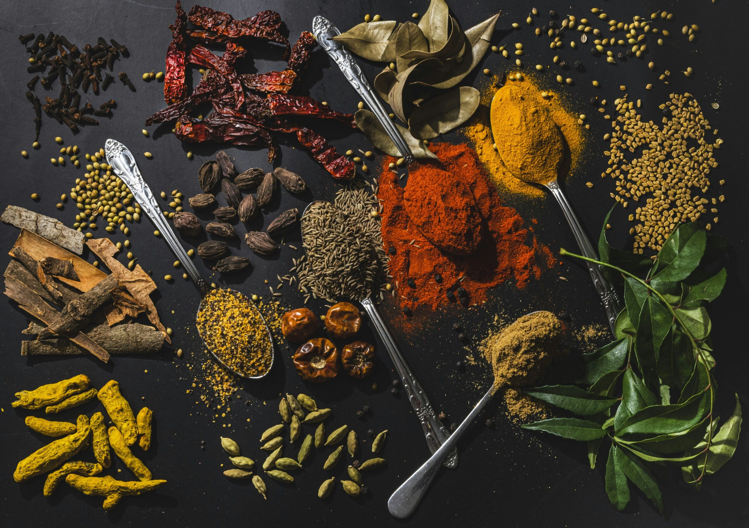 An assortment of whole and ground spices on a dark surface