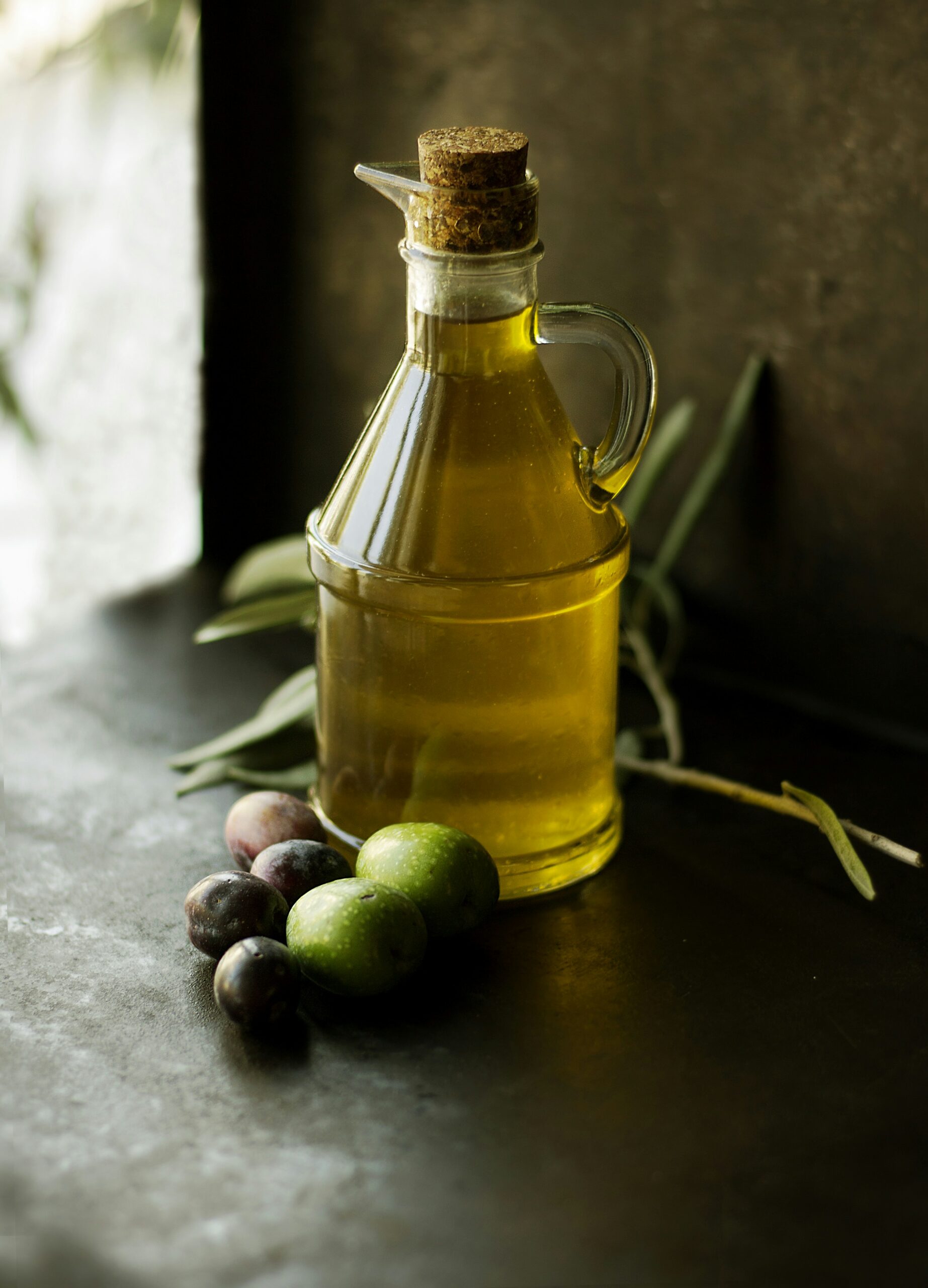 A glass bottle of olive oil alongside olives