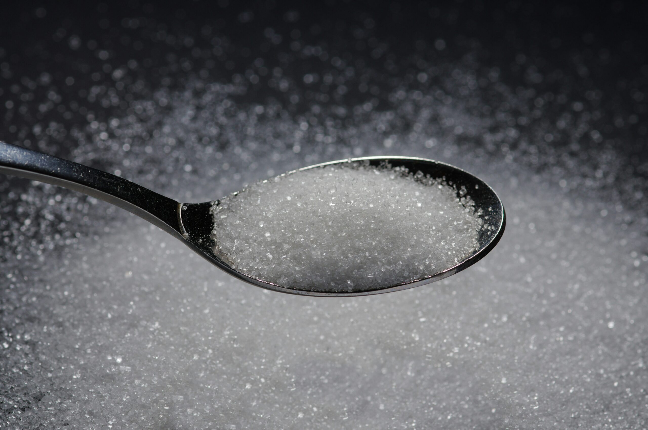 White sugar crystals in a spoon on a dark surface